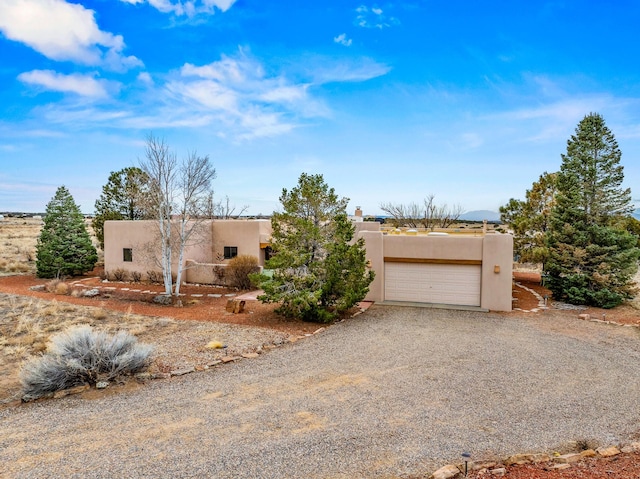 pueblo-style home with stucco siding, an attached garage, and driveway