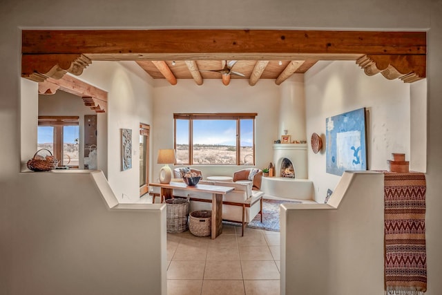 living room with plenty of natural light, a lit fireplace, beam ceiling, and light tile patterned flooring