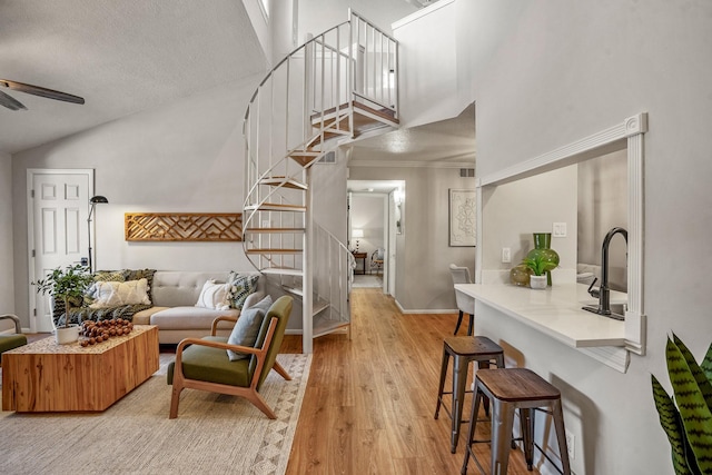 living area with stairway, ceiling fan, high vaulted ceiling, and light wood-style floors