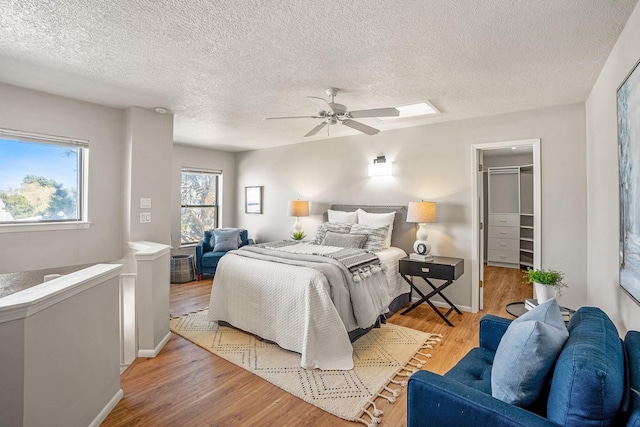 bedroom featuring a walk in closet, a ceiling fan, a textured ceiling, wood finished floors, and baseboards