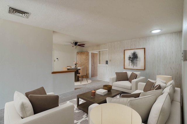 carpeted living room with visible vents, a textured ceiling, and a ceiling fan