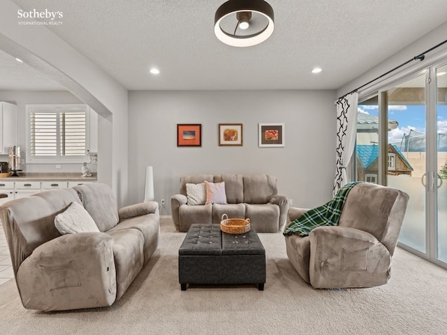 living area featuring arched walkways, light colored carpet, and a textured ceiling