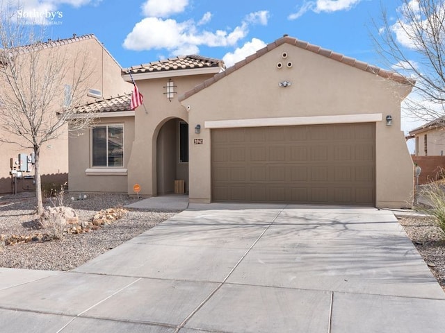 mediterranean / spanish-style home with a tile roof, an attached garage, concrete driveway, and stucco siding