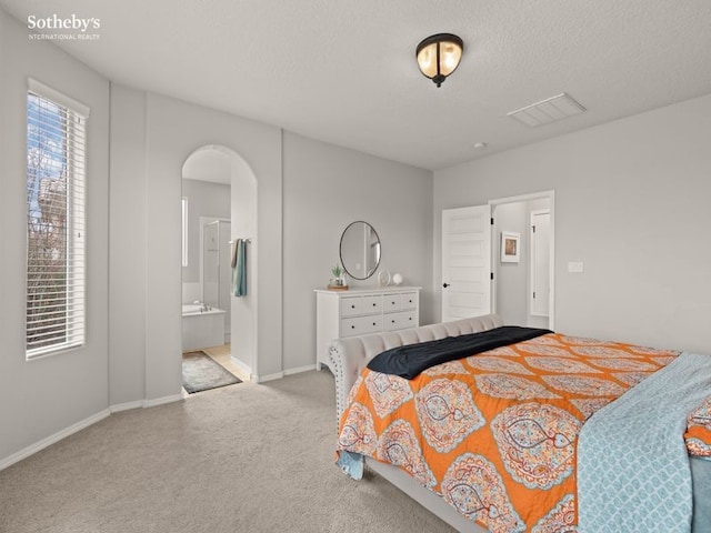 carpeted bedroom with baseboards, visible vents, arched walkways, a textured ceiling, and connected bathroom