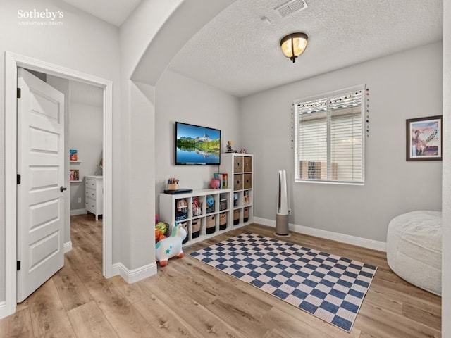 rec room featuring wood finished floors, arched walkways, visible vents, and baseboards