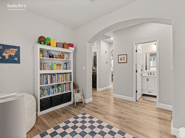 living area with arched walkways, light wood-style flooring, a textured ceiling, and baseboards