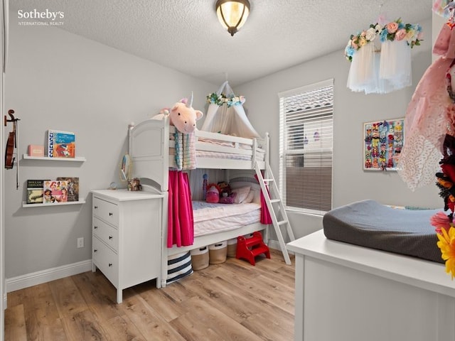 bedroom with baseboards, a textured ceiling, and light wood-style floors