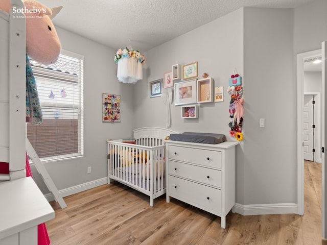 bedroom with baseboards, a nursery area, light wood-style flooring, and a textured ceiling