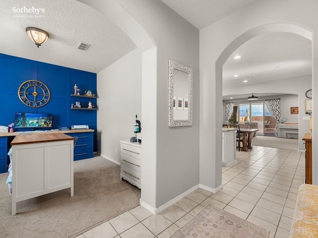 hall featuring arched walkways, light tile patterned floors, a textured ceiling, and baseboards