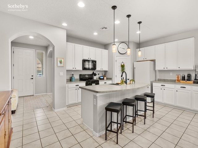 kitchen featuring a kitchen bar, light tile patterned floors, arched walkways, black appliances, and a sink