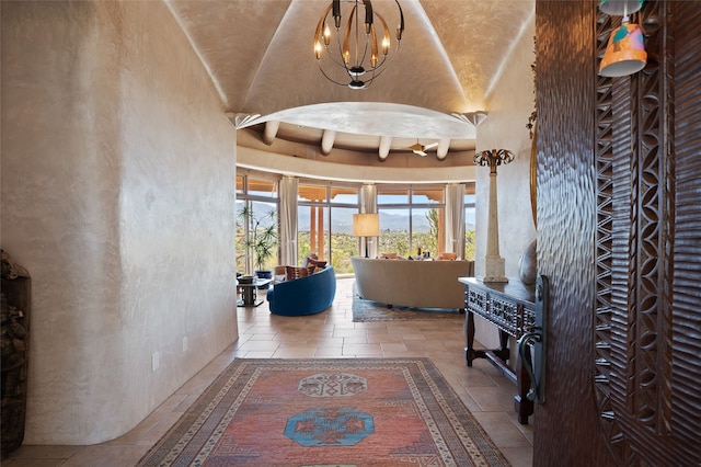 hallway with stone tile floors, an inviting chandelier, and a towering ceiling