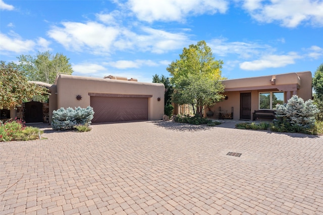 pueblo revival-style home with stucco siding, an attached garage, decorative driveway, and a gate