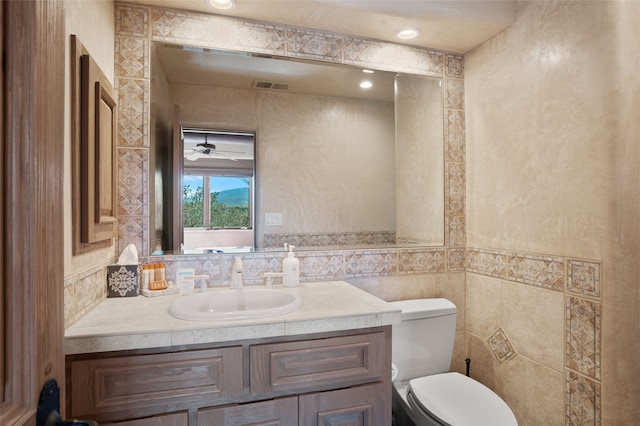 half bath with visible vents, toilet, tile walls, and vanity