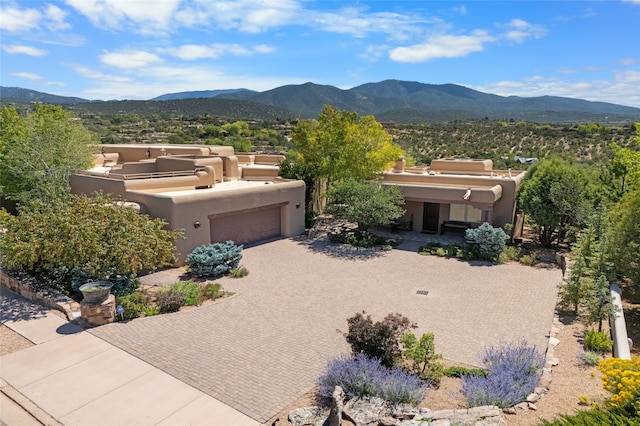 pueblo-style home featuring an outdoor living space, stucco siding, a garage, decorative driveway, and a mountain view