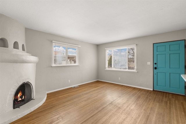 unfurnished living room with a wealth of natural light, visible vents, a brick fireplace, and wood finished floors