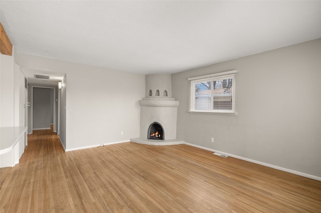 unfurnished living room featuring visible vents, a fireplace, baseboards, and light wood-style floors