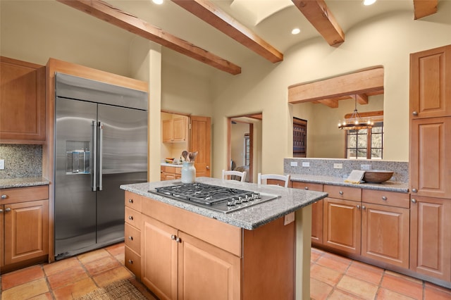 kitchen featuring light stone countertops, appliances with stainless steel finishes, beamed ceiling, backsplash, and a center island