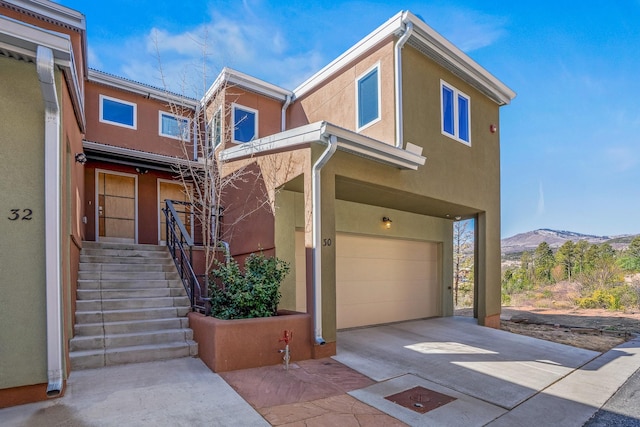 multi unit property featuring concrete driveway, a garage, a mountain view, and stucco siding