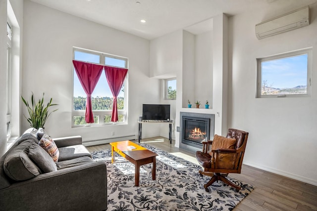 living area with a wall unit AC, a tiled fireplace, wood finished floors, baseboards, and a baseboard heating unit