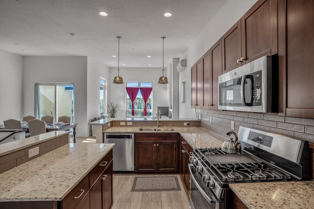 kitchen featuring light wood finished floors, a peninsula, a sink, appliances with stainless steel finishes, and backsplash