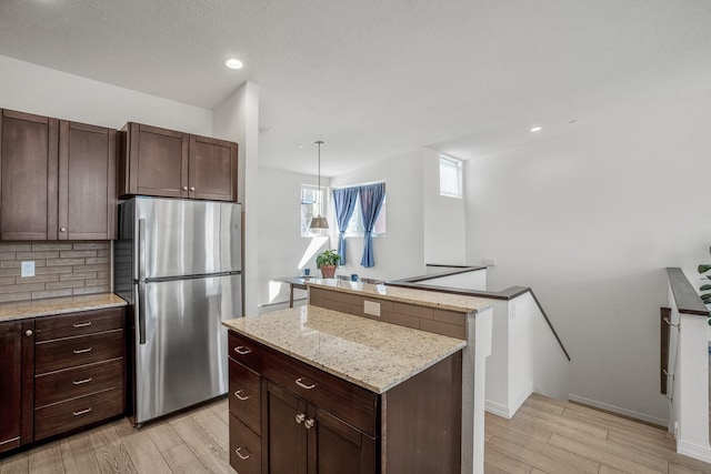 kitchen with decorative backsplash, light wood finished floors, a kitchen island, and freestanding refrigerator