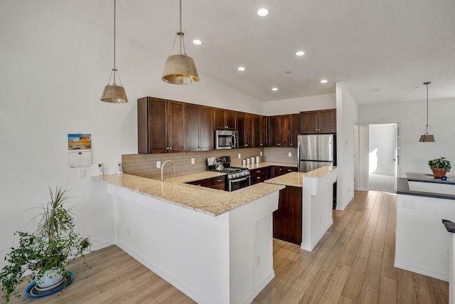 kitchen with a peninsula, stainless steel appliances, light wood-type flooring, and light stone countertops