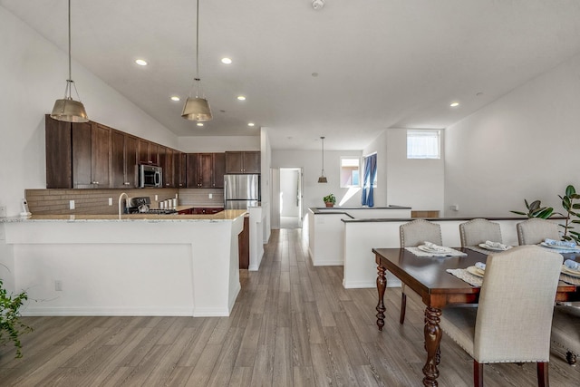 kitchen with a peninsula, light wood-style flooring, tasteful backsplash, and appliances with stainless steel finishes