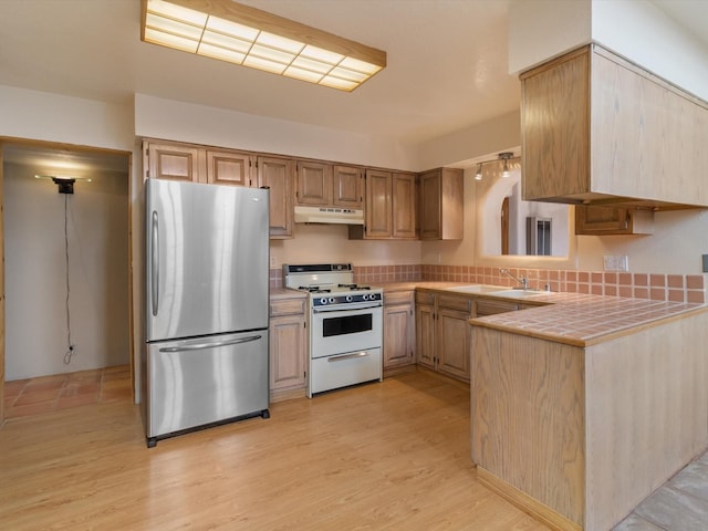 kitchen featuring under cabinet range hood, tile countertops, white range with gas cooktop, freestanding refrigerator, and a sink