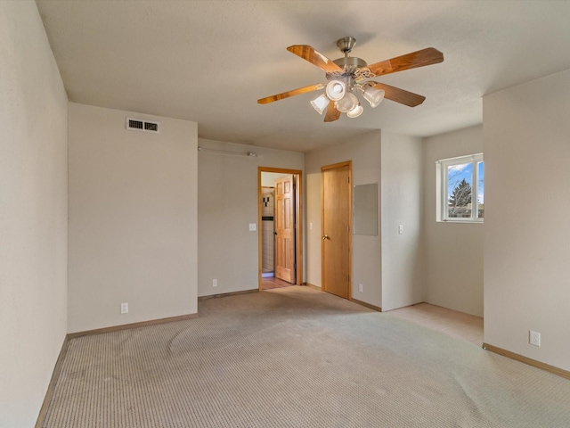 empty room featuring a ceiling fan, light colored carpet, visible vents, and baseboards