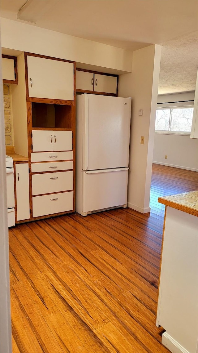 kitchen with light wood-style flooring, freestanding refrigerator, light countertops, baseboards, and stove