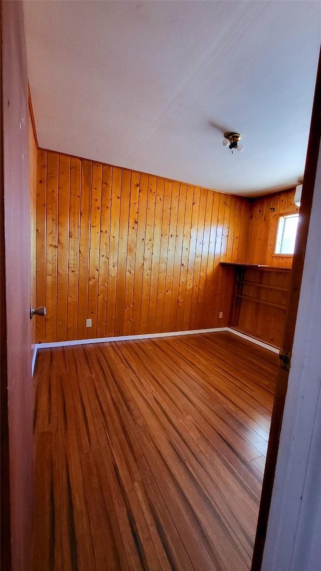 unfurnished room featuring wood finished floors, baseboards, and wood walls