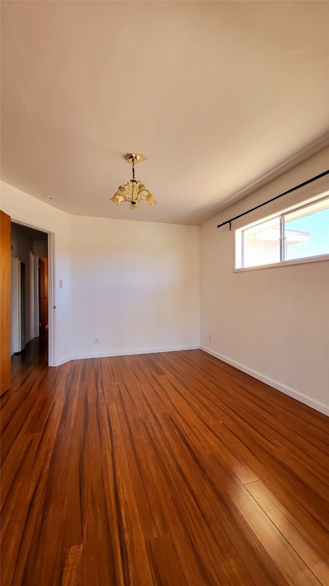 unfurnished room featuring a notable chandelier, baseboards, and wood finished floors