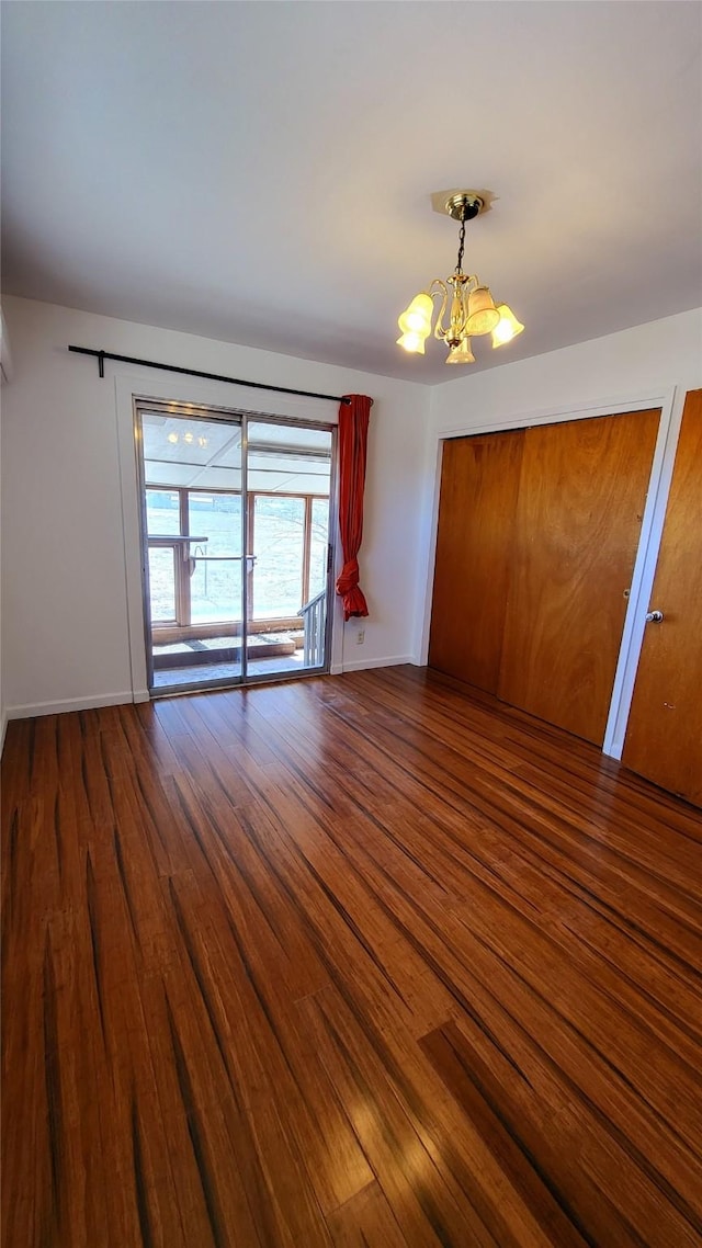 empty room with an inviting chandelier, wood finished floors, and baseboards