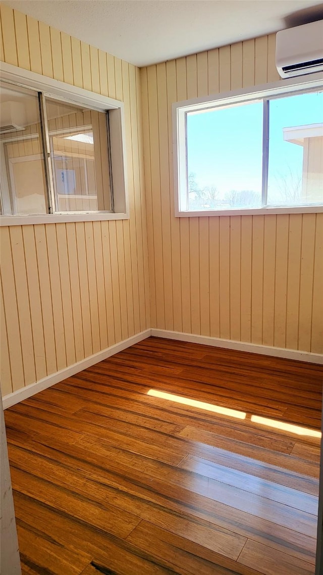 unfurnished room featuring wood finished floors, baseboards, and a wall mounted air conditioner