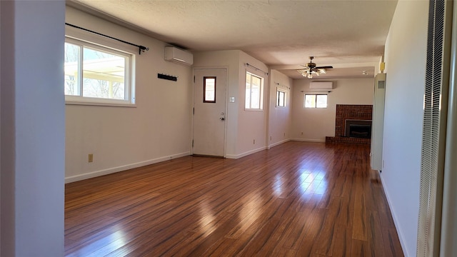 unfurnished living room featuring an AC wall unit, hardwood / wood-style flooring, a textured ceiling, a wall unit AC, and a brick fireplace