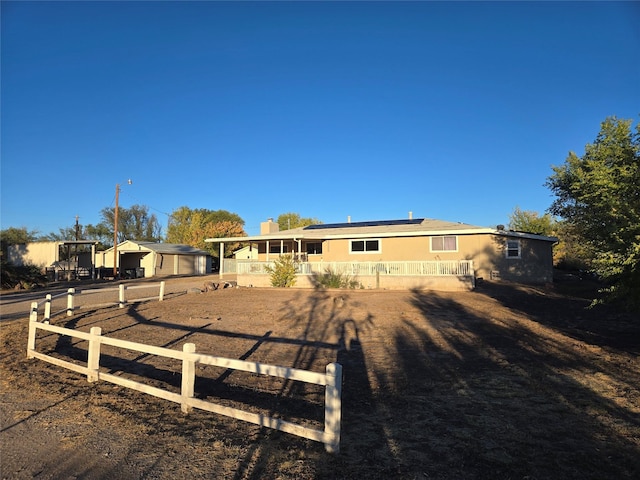 back of house with roof mounted solar panels, covered porch, and fence