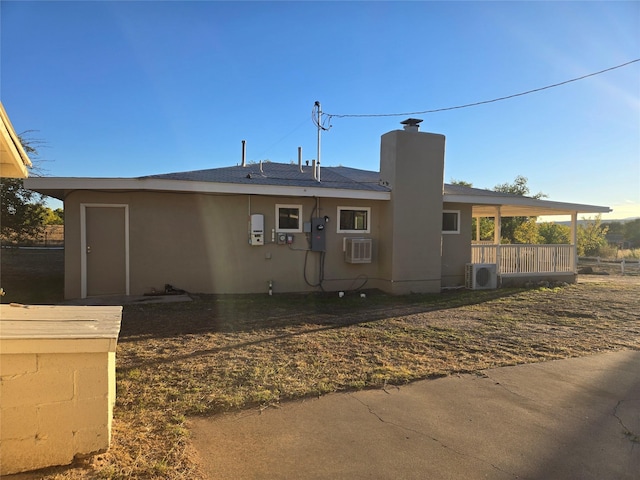 view of front facade featuring a wall mounted air conditioner, stucco siding, ac unit, and a chimney