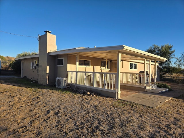 back of house featuring covered porch, a chimney, and ac unit