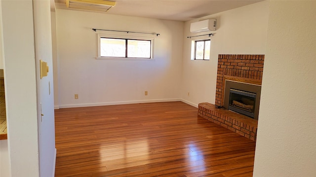 unfurnished living room featuring visible vents, baseboards, a wall mounted air conditioner, hardwood / wood-style floors, and a fireplace