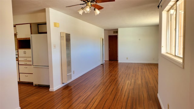 unfurnished room featuring ceiling fan, baseboards, wood finished floors, and a heating unit