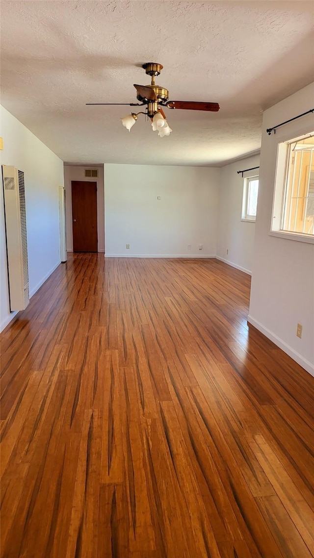 unfurnished room featuring a ceiling fan, wood finished floors, baseboards, and a textured ceiling