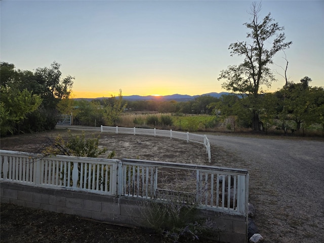 yard at dusk featuring a mountain view and fence