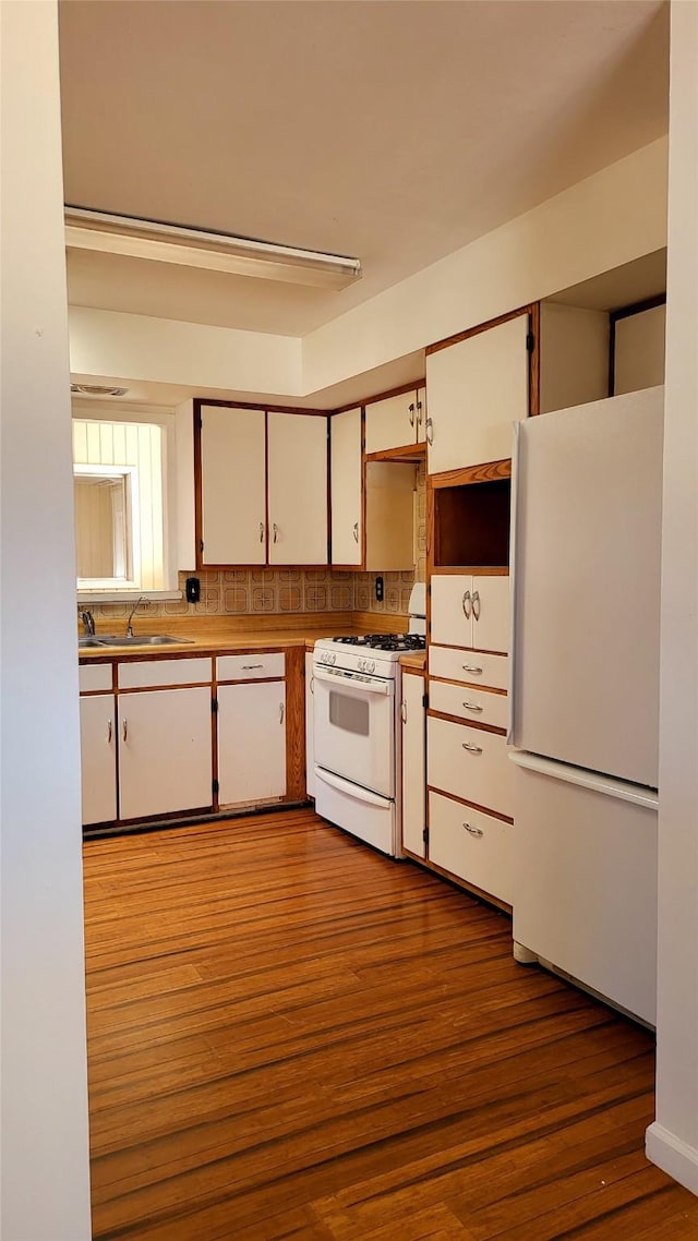 kitchen with white appliances, white cabinets, wood finished floors, and a sink