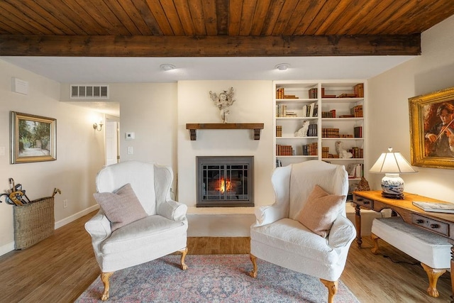 living area with beam ceiling, visible vents, and wood finished floors