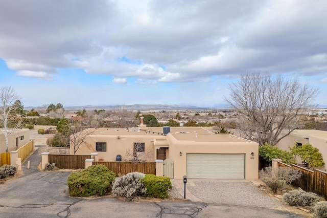 southwest-style home with driveway, an attached garage, a chimney, stucco siding, and a fenced front yard