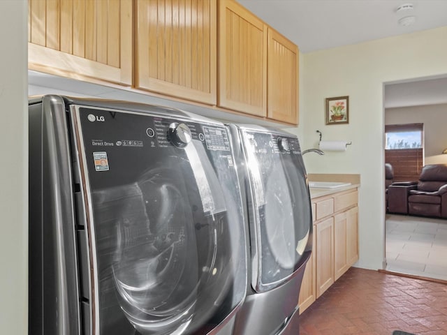 laundry area featuring a sink, cabinet space, brick floor, and washer and clothes dryer