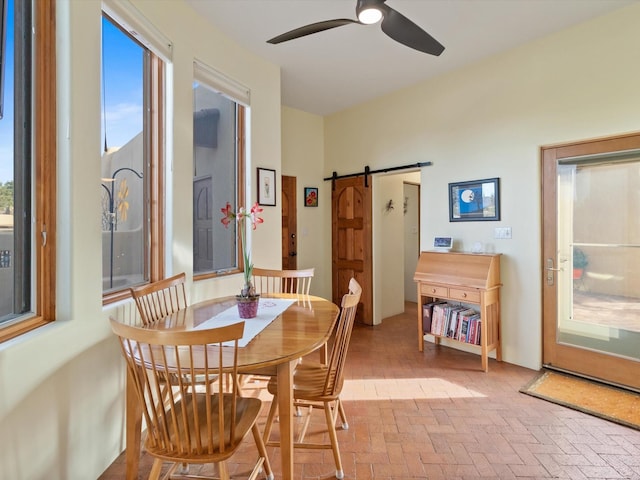 dining space featuring brick floor, a barn door, and a ceiling fan