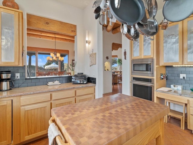 kitchen featuring an inviting chandelier, stainless steel appliances, decorative backsplash, glass insert cabinets, and butcher block counters