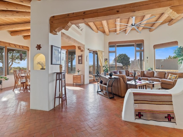 living area featuring beamed ceiling, ceiling fan, wood ceiling, and brick floor