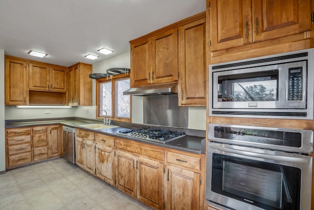 kitchen featuring light floors, a sink, stainless steel appliances, under cabinet range hood, and dark countertops